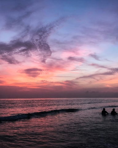 Family silhouettes on a Florida Gulf Coast beach at sunset with vivid pink and purple sky