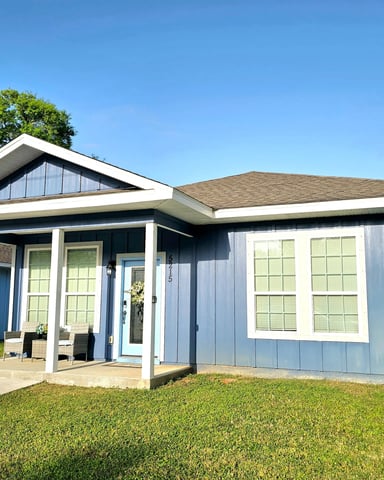 Modern single-story house with light blue siding, white trim, covered porch, and attached garage under clear blue sky